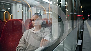 Relaxed woman boring train looking window at station platform. Shaved head girl