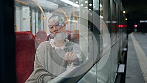 Relaxed woman boring train looking window at station platform. Shaved head girl