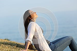 Relaxed woman breathing fresh air sitting on the grass