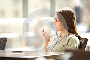 Relaxed woman contemplating drinking coffee in a bar