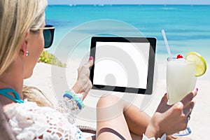 Relaxed woman drinking cocktail and holding tablet computer on the beach