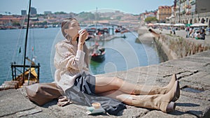 Relaxed woman drinking coffee sunny river embankment. Lady enjoying work break