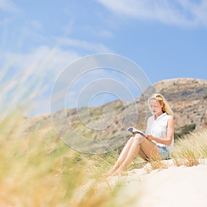 Woman reading book, enjoying sun on beach.