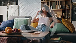 Relaxed woman freelancer drinking tea sitting cozy couch living room alone.