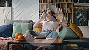 Relaxed woman freelancer drinking tea sitting cozy couch living room alone.