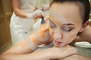 Relaxed woman having clay body mask apply by beautician