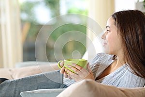 Relaxed woman holding coffee mug contemplating through window photo