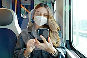 Relaxed woman with KN95 FFP2 face mask using smart phone app. Train passenger with protective mask traveling sitting texting on
