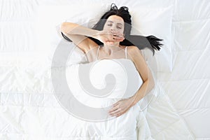 Relaxed woman lies on large white bed and yawns