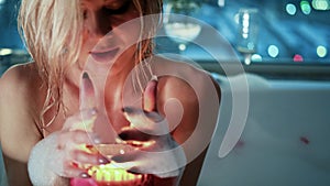 Relaxed woman lighting a candle while taking a bubble bath in the evening.