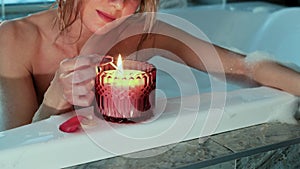 Relaxed woman lighting a candle while taking a bubble bath in the evening.