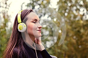 Young happy woman listening music from smartphone with headphones in a quiet Park