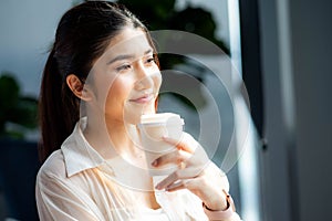 Relaxed woman looking away drinking coffee at home looking out the window enjoying the new day