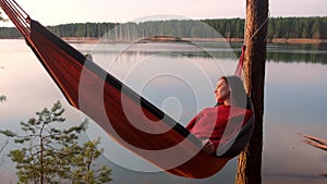 Relaxed woman lying in hammock in forest enjoy admiring lake nature at sunset.