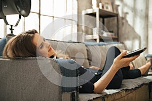 Relaxed woman lying on sofa and watching tv in loft apartment