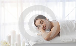Relaxed woman lying in spa salon with closed eyes, waiting for massage