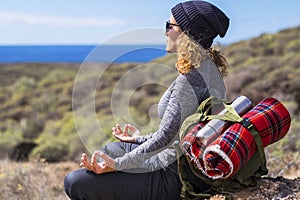 Relaxed woman in meditation position sitting on the rocks during travel backpack adventure leisure activity outdoor. Adult female