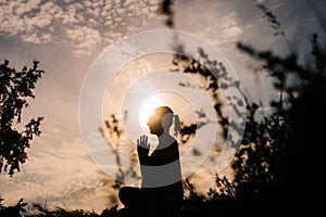 Relaxed woman is performing namaste yoga pose background of sun outdoor on park outside city evening