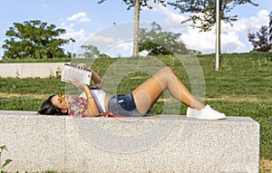 Relaxed woman reading a book while lying on a bench in a park