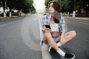 Relaxed woman sitting in the middle of an empty city road, phone in hand