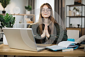 Relaxed woman sitting on workplace with modern laptop and meditating with closed eyes