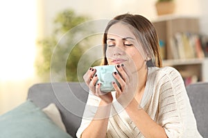 Relaxed woman smelling coffee on a couch at home photo