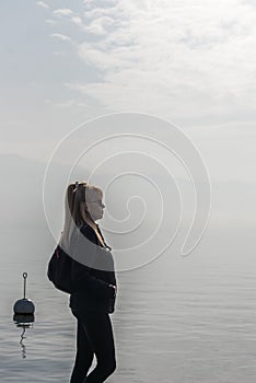 Relaxed woman standing near lake while contemplating the nature view on a misty day.