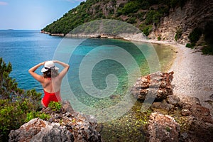 Beautiful curly girl sitting on the beach, vacation mood. Relaxed woman thinking looking away on the beach. Red bikini and hat