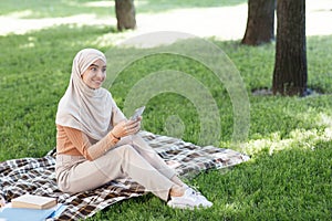 Relaxed woman using mobile phone in city park, sending text messages and chatting