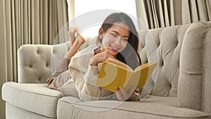 Relaxed woman in warm sweater reading book on couch, spending leisure time in cozy winter or autumn weekend