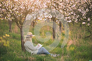 Relaxed woman is writing her diary and resting in blooming cherry orchard