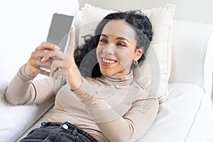 Relaxed young African American woman using crucial mobile phone on sofa couch