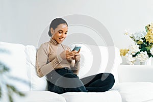 Relaxed young African American woman using crucial mobile phone on sofa couch