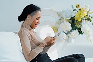 Relaxed young African American woman using crucial mobile phone on sofa couch