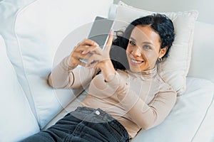 Relaxed young African American woman using crucial mobile phone on sofa couch