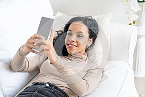 Relaxed young African American woman using crucial mobile phone on sofa couch