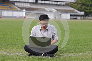 Relaxed young Asian business man working with laptop on green grass.