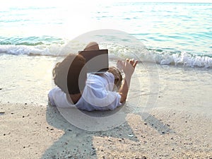 Relaxed young Asian man with laptop lying down on the beach. Summer vacations concept.
