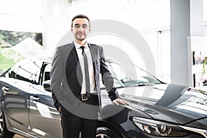 Relaxed young businessman or salesman with hands crossed in front of car