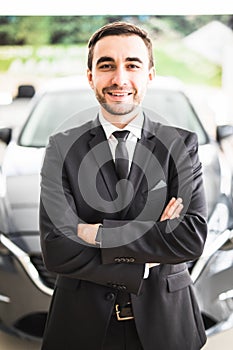 Relaxed young businessman or salesman with hands crossed in front of car
