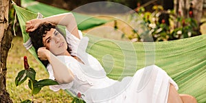 Relaxed young caucasian woman looking at camera lying in hammock in backyard of country house.