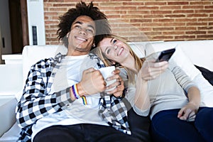 Relaxed young couple changing channels with the remote control while watching TV on the sofa at home