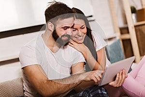 Relaxed young couple using digital tablet in bed at home