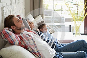 Relaxed young family resting and dreaming about new home on comfortable sofa together at home