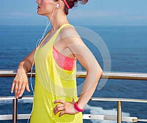 Relaxed young fitness woman listening to music at embankment