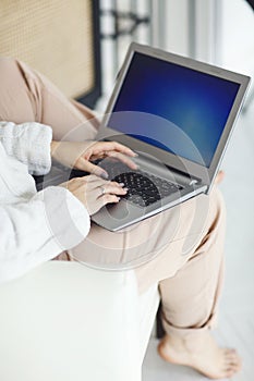 Relaxed young girl sitting in chair at home with laptop computer on her laps, close up of the female hands