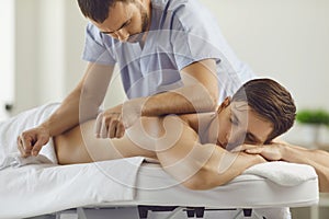 Relaxed young man enjoying remedial body massage in spa salon or wellness center photo