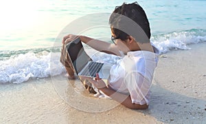 Relaxed young man with laptop sitting on the sandy beach with soft waves. Internet of things concept