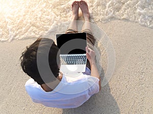 Relaxed young man with laptop sitting on the sandy beach with soft waves. Internet of things concept