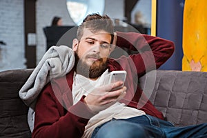 Relaxed young man lying on sofa and using cellphone